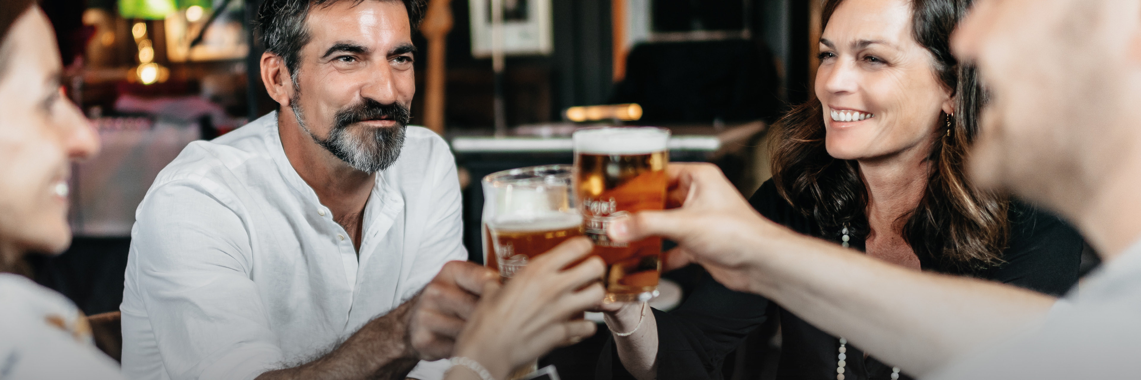 Vier junge Menschen prosten sich mit Bier zu. Es herrscht eine ausgelassene Stimmung.