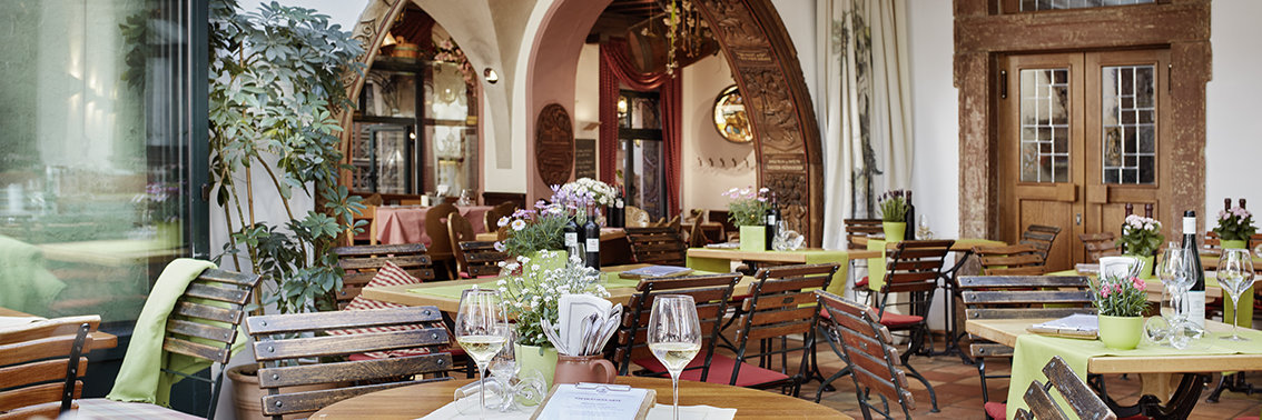 Blick von der Terrasse ins Restaurant vom Breuer's Rüdesheimer Schloss. Das Ambiente sieht sehr gemütlich und einladend aus. Auf den Tischen stehen frische Blumen