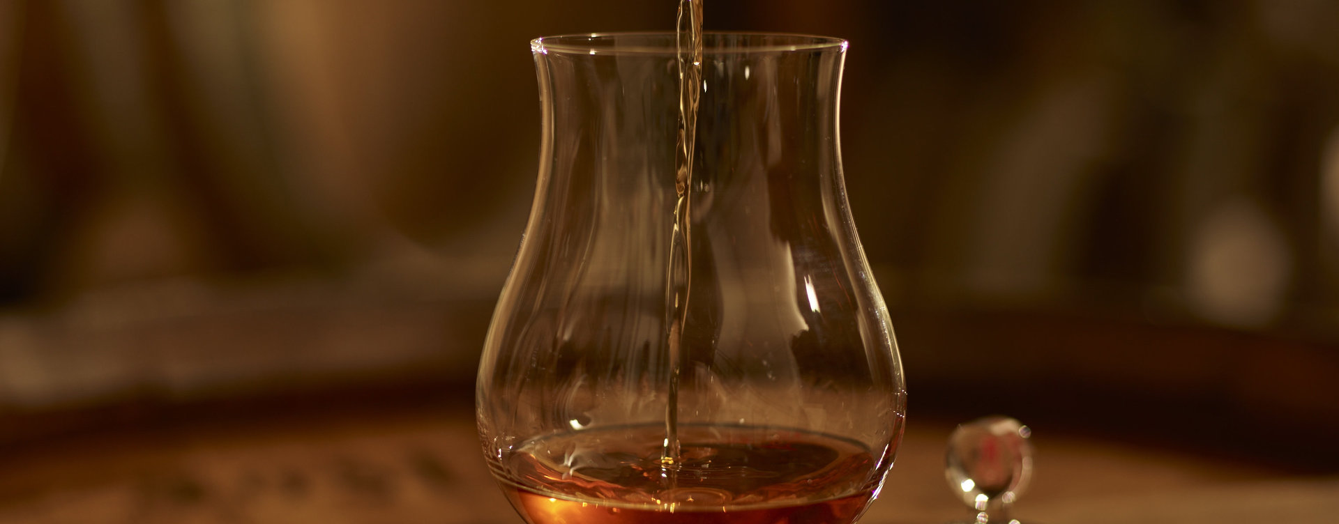 In einem dunklen Raum wird Asbach in ein spezielles Glas ausgeschänkt. Das Glas steht auf einem Weinfass.