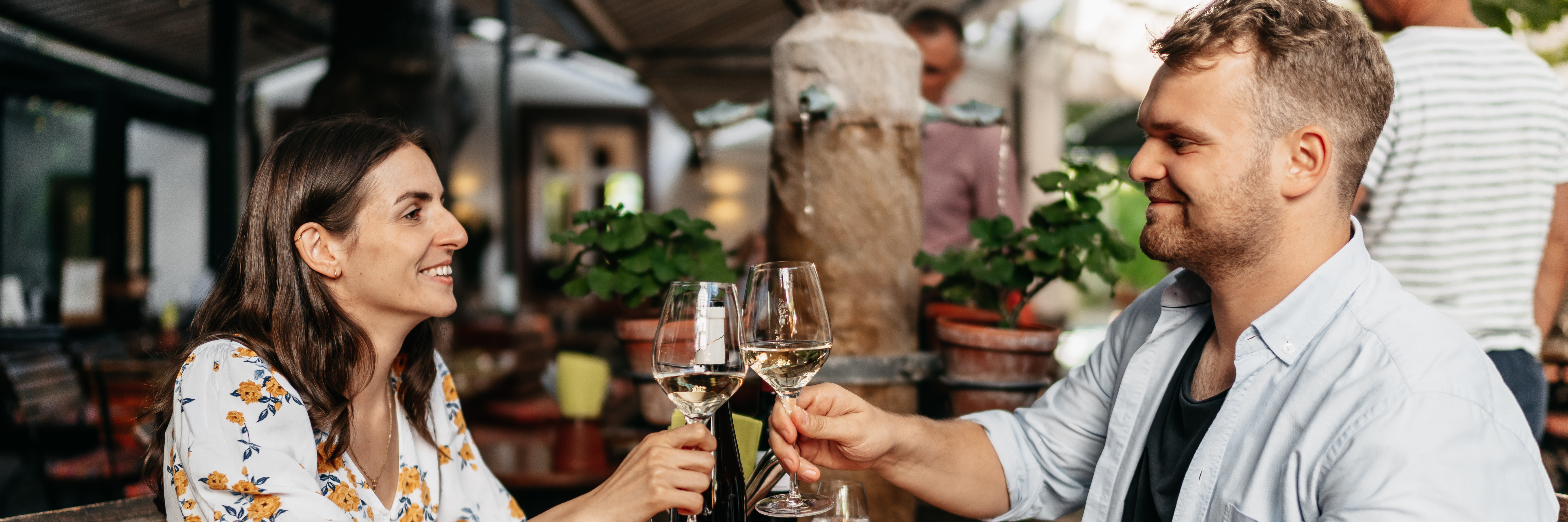 Ein Pärchen sitzt in einem Restaurant. Sie stoßen mit einem Glas Weißwein von Weingut Georg Breuer an. 