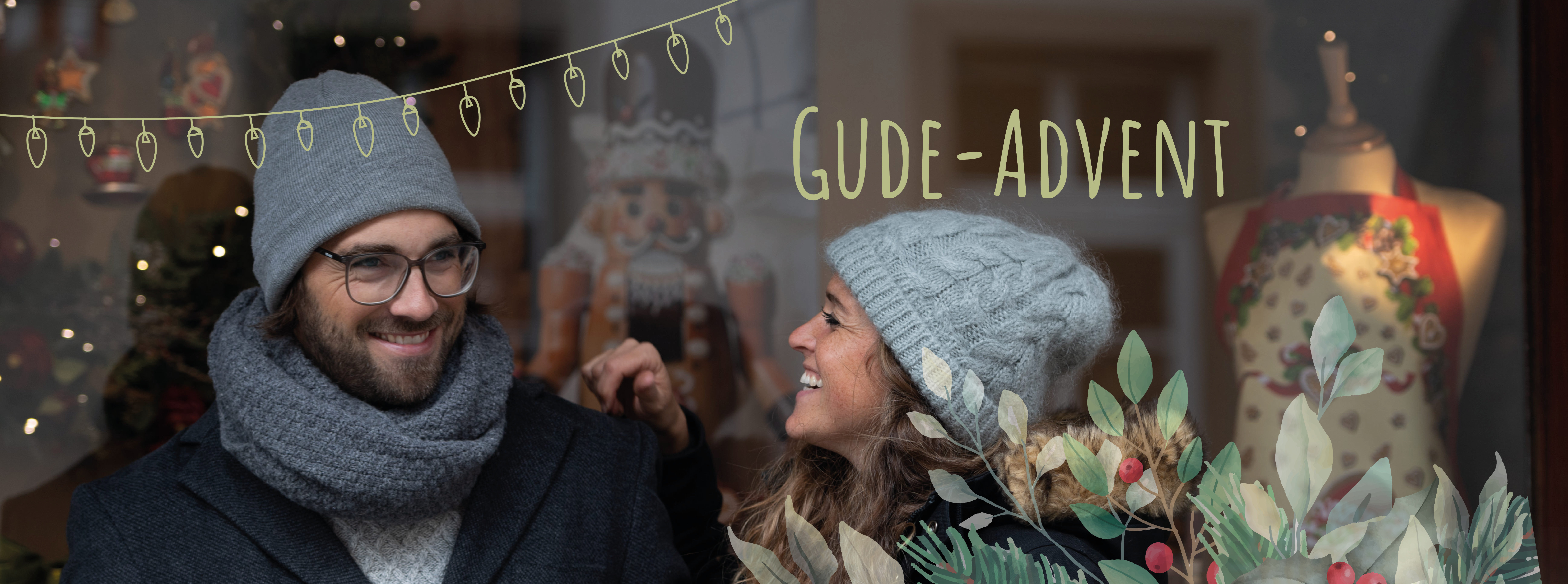 Ein Paar steht mit Glühwein in der Hand vor einem weihnachtlich geschmückten Schaufenster
