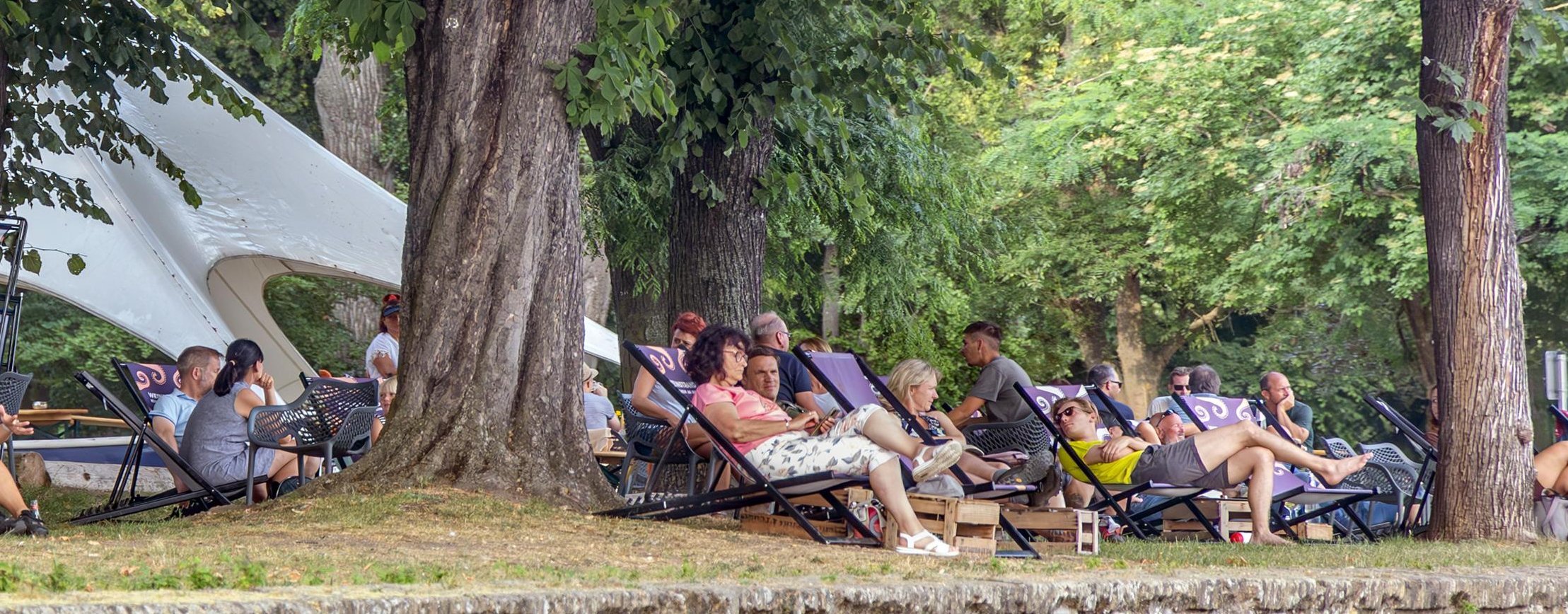 Der Hafenpark in Rüdesheim an einem schönen Sommertag. Viele Gäste sitzen auf Liegestühlen und genießen Ihre Getränke.