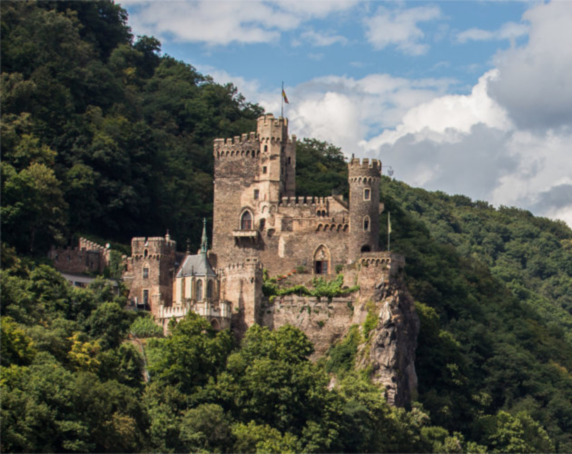 Die Burg Rheinstein gegenüber von Assmannshausen. Im Hintergrund sieht man einen Wald und es ist schönes Wetter.