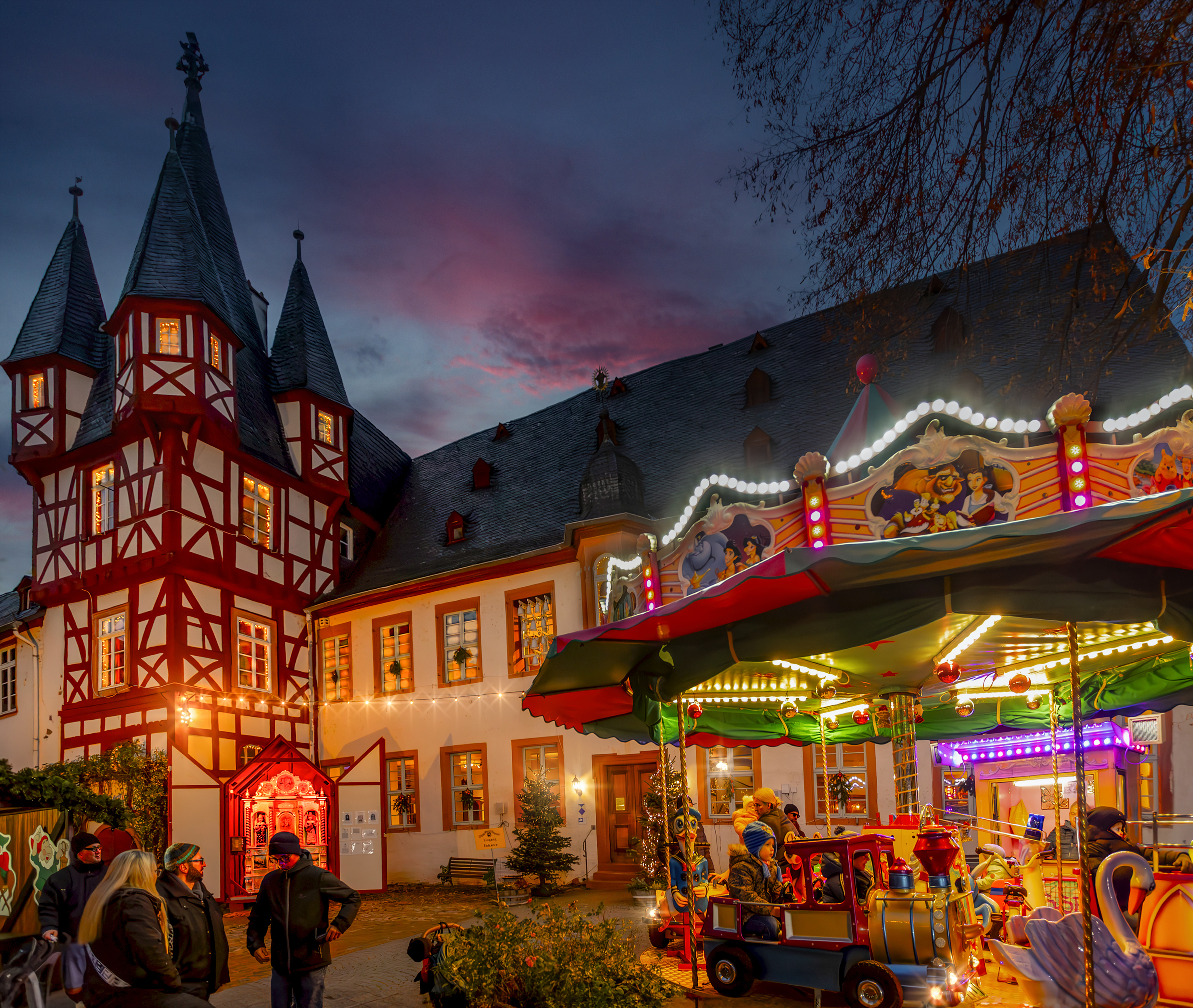 Siegfrieds Mechanisches Musikkabinett ist hell erleuchtet am Abend. Ein Karussel steht vor dem Eingang.