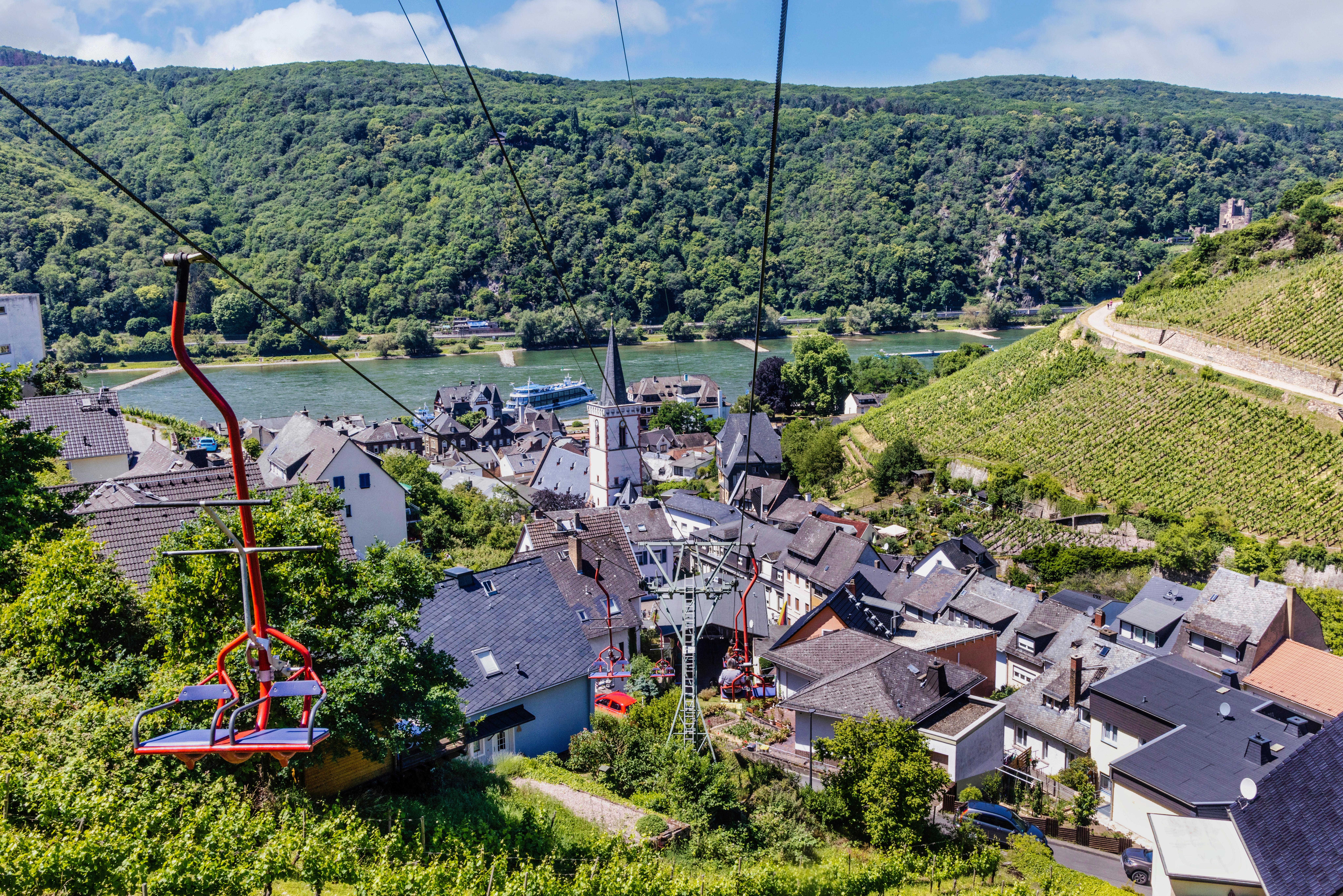 Die roten Sitze der Sesselliftbahn Assmannshausen schweben über Assmannshausen mit einem atemberaubenden Ausblick auf die Naturlandschaft und den Rhein.